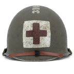 US M1 Combat-Medic-Helm, McCord-Helmglocke 970A, Vorderansicht, rotes Kreuz auf quadratischem weissem Feld und hochgeschlagener Lederkinnriemen des Innenhelms